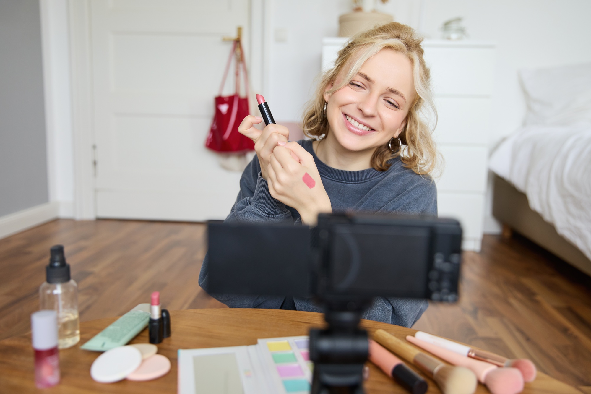 Portrait of young creative social media content creator, woman showing lipstick swatches on her